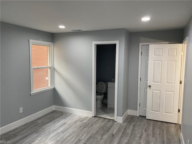 unfurnished bedroom with ensuite bath, a closet, and wood-type flooring