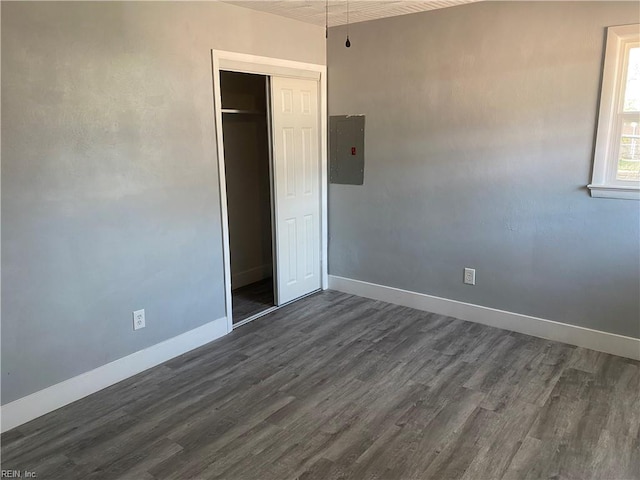 unfurnished bedroom with dark wood-type flooring, electric panel, and a closet