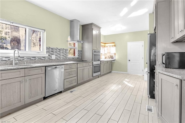 kitchen featuring light stone countertops, appliances with stainless steel finishes, tasteful backsplash, sink, and range hood