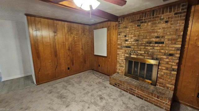 unfurnished living room with carpet, a fireplace, beam ceiling, and wood walls