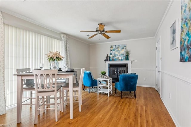 dining room featuring ceiling fan, a fireplace, hardwood / wood-style flooring, and ornamental molding