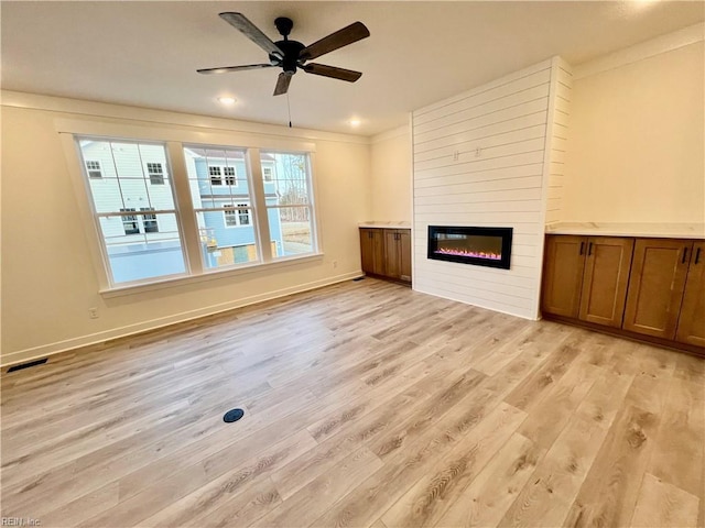 unfurnished living room featuring ceiling fan, a large fireplace, a healthy amount of sunlight, and light hardwood / wood-style flooring