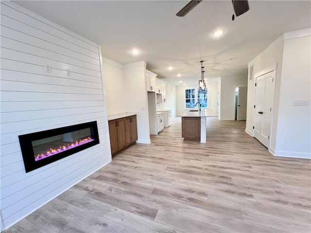 unfurnished living room featuring a large fireplace, light hardwood / wood-style floors, ceiling fan, and sink