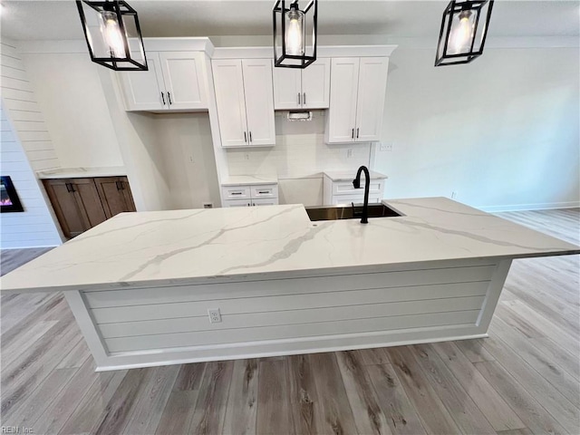 kitchen with white cabinets, pendant lighting, a kitchen island with sink, and sink