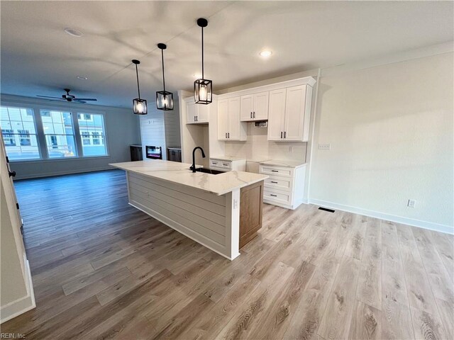 kitchen with white cabinets, a center island with sink, sink, hanging light fixtures, and light wood-type flooring