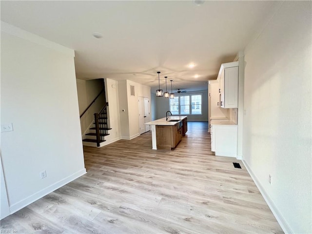 kitchen with a center island with sink, white cabinets, pendant lighting, and light hardwood / wood-style floors