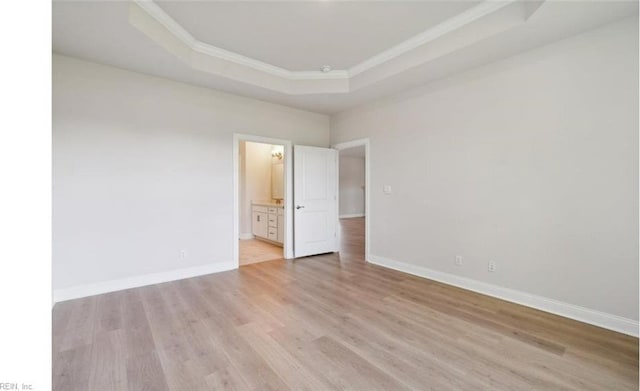 unfurnished bedroom with a raised ceiling, ornamental molding, connected bathroom, and light hardwood / wood-style flooring