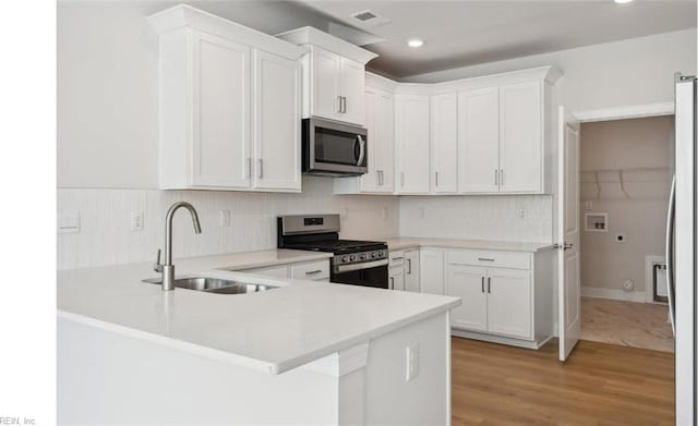 kitchen featuring kitchen peninsula, appliances with stainless steel finishes, sink, white cabinets, and light hardwood / wood-style floors