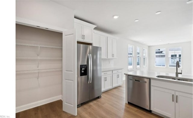 kitchen with sink, light hardwood / wood-style flooring, decorative backsplash, appliances with stainless steel finishes, and white cabinetry