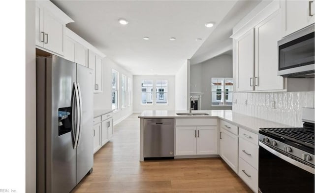 kitchen with kitchen peninsula, white cabinetry, sink, and appliances with stainless steel finishes