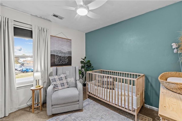 carpeted bedroom featuring ceiling fan and a crib