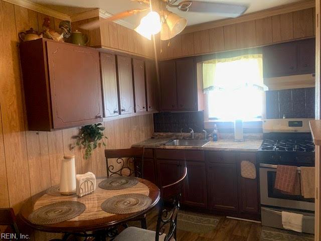 kitchen featuring stainless steel stove, ceiling fan, wooden walls, and sink