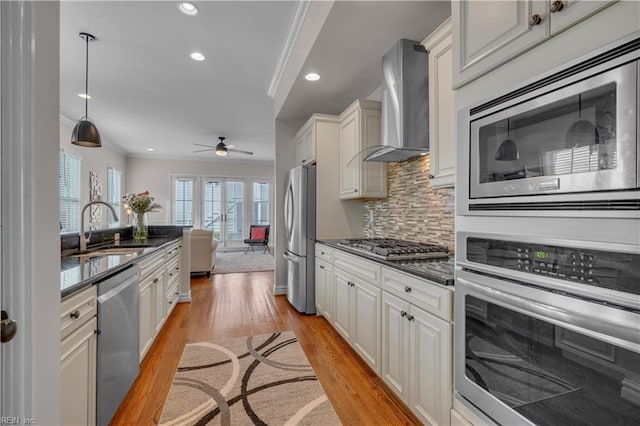 kitchen with sink, wall chimney exhaust hood, stainless steel appliances, backsplash, and ornamental molding