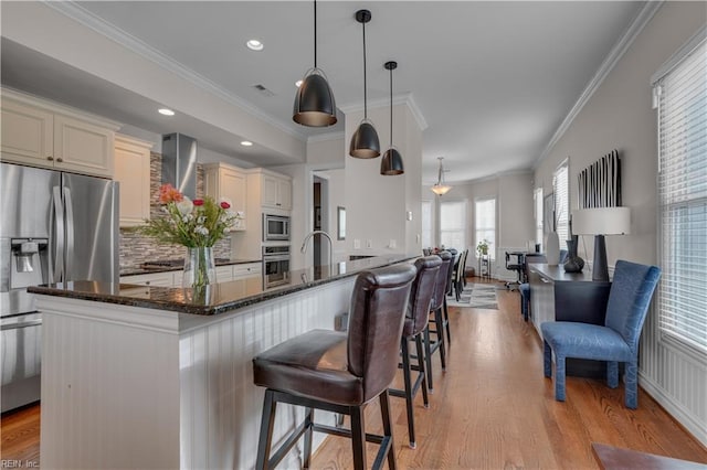 kitchen featuring crown molding, hanging light fixtures, dark stone countertops, a kitchen bar, and stainless steel appliances