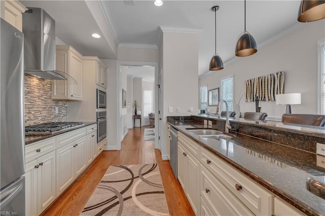 kitchen with dark stone counters, stainless steel appliances, sink, wall chimney range hood, and pendant lighting