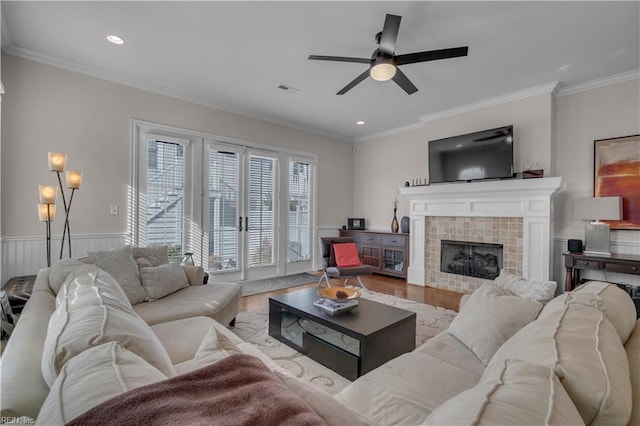 living room featuring ceiling fan, french doors, light hardwood / wood-style floors, a tiled fireplace, and ornamental molding