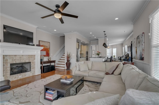 living room featuring a tiled fireplace, crown molding, a wealth of natural light, and light hardwood / wood-style flooring