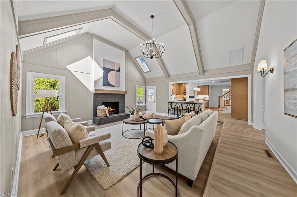 living room with a fireplace, high vaulted ceiling, a chandelier, and light hardwood / wood-style floors