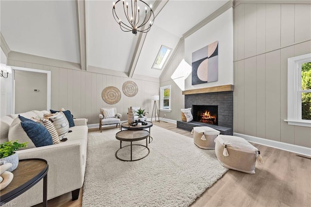 living room with a chandelier, light hardwood / wood-style floors, and vaulted ceiling with skylight