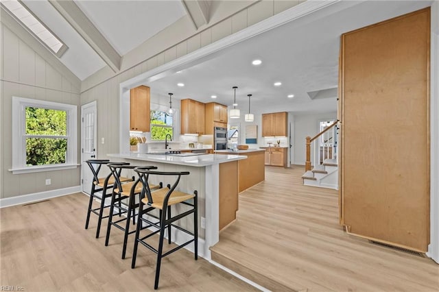 kitchen featuring a kitchen bar, sink, light hardwood / wood-style flooring, a kitchen island, and hanging light fixtures