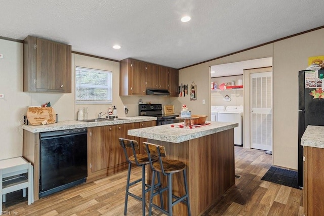 kitchen featuring crown molding, sink, washer and dryer, black appliances, and light hardwood / wood-style floors