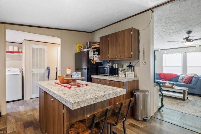 kitchen with black refrigerator, ceiling fan, a kitchen island, dark hardwood / wood-style flooring, and a breakfast bar area