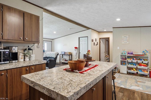 kitchen with a center island, dark hardwood / wood-style flooring, a textured ceiling, a breakfast bar, and ornamental molding