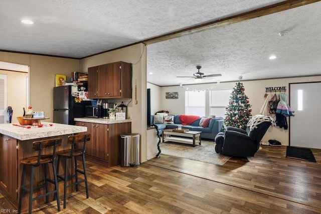 kitchen with a kitchen breakfast bar, ceiling fan, stainless steel fridge, a textured ceiling, and dark hardwood / wood-style flooring