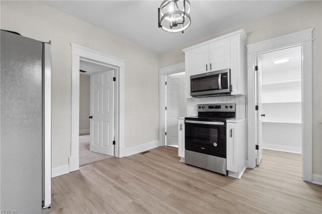 kitchen featuring white cabinets, appliances with stainless steel finishes, light hardwood / wood-style floors, and an inviting chandelier