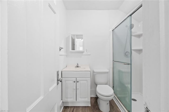 bathroom featuring hardwood / wood-style flooring, vanity, a shower with shower door, and toilet