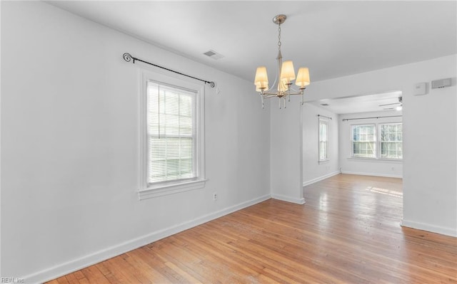 empty room featuring a wealth of natural light, ceiling fan with notable chandelier, and light wood-type flooring