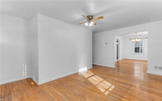 spare room with ceiling fan with notable chandelier and light wood-type flooring