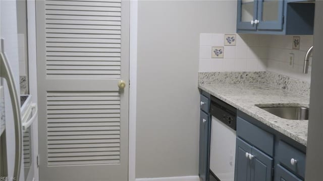 kitchen with decorative backsplash, light stone counters, white dishwasher, and blue cabinets