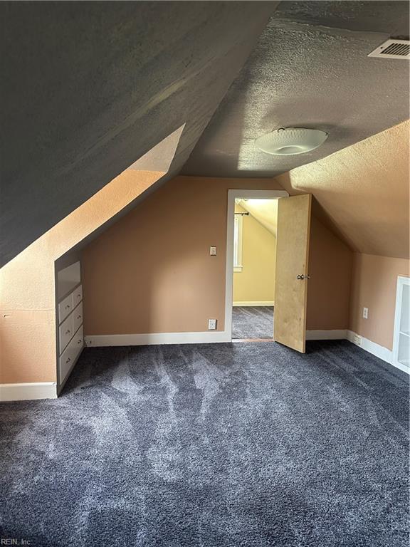 bonus room with dark colored carpet, lofted ceiling, and a textured ceiling