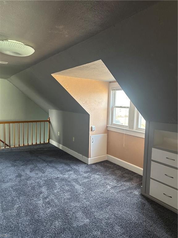 additional living space featuring a textured ceiling, dark carpet, and vaulted ceiling