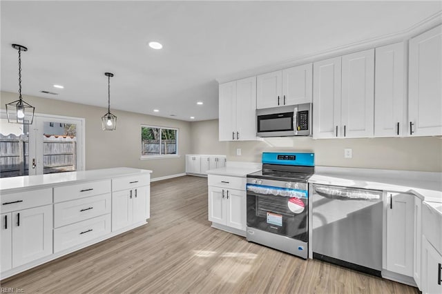 kitchen featuring light wood-type flooring, white cabinetry, stainless steel appliances, and hanging light fixtures