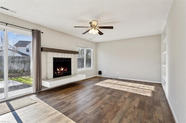 unfurnished living room with a textured ceiling, dark hardwood / wood-style flooring, ceiling fan, and a tiled fireplace