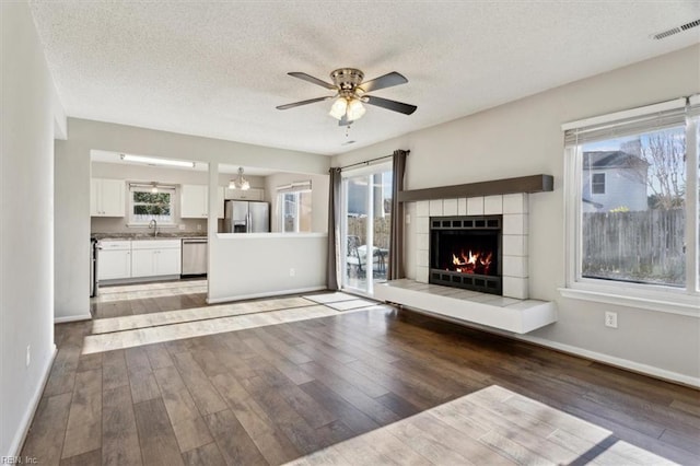 unfurnished living room with a tile fireplace, wood-type flooring, plenty of natural light, and sink