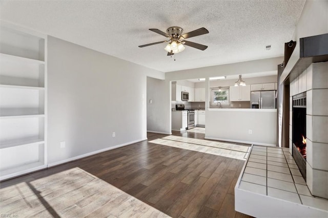 unfurnished living room with a textured ceiling, ceiling fan, a tile fireplace, light hardwood / wood-style flooring, and built in features