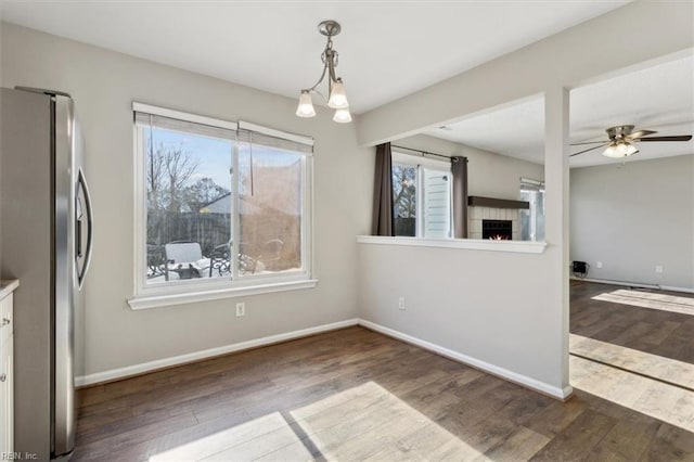 unfurnished dining area with ceiling fan with notable chandelier and dark hardwood / wood-style flooring