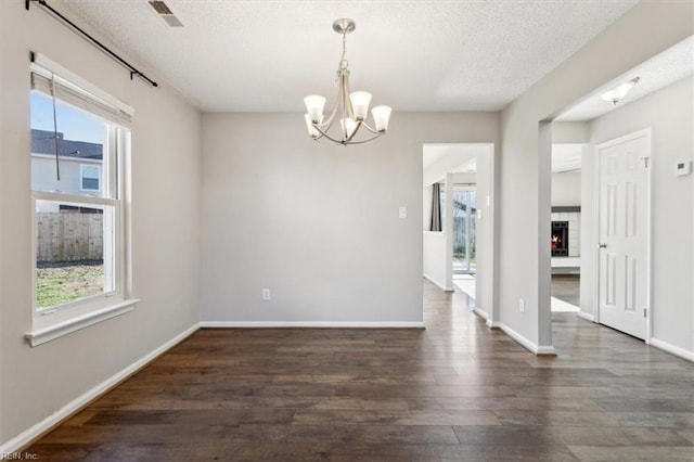 unfurnished dining area with a wealth of natural light, dark hardwood / wood-style flooring, a chandelier, and a textured ceiling