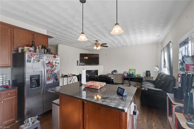 kitchen with hanging light fixtures, ceiling fan, stainless steel fridge, dark stone countertops, and dark hardwood / wood-style flooring