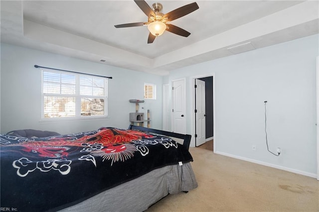 carpeted bedroom featuring a tray ceiling and ceiling fan