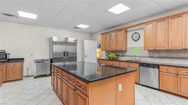 kitchen featuring a paneled ceiling, dark stone counters, sink, an island with sink, and appliances with stainless steel finishes