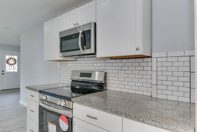 kitchen featuring white cabinets, light wood-type flooring, light stone countertops, tasteful backsplash, and stainless steel appliances