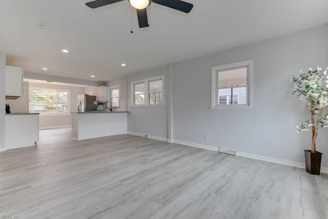 unfurnished living room with ceiling fan, sink, and light hardwood / wood-style floors