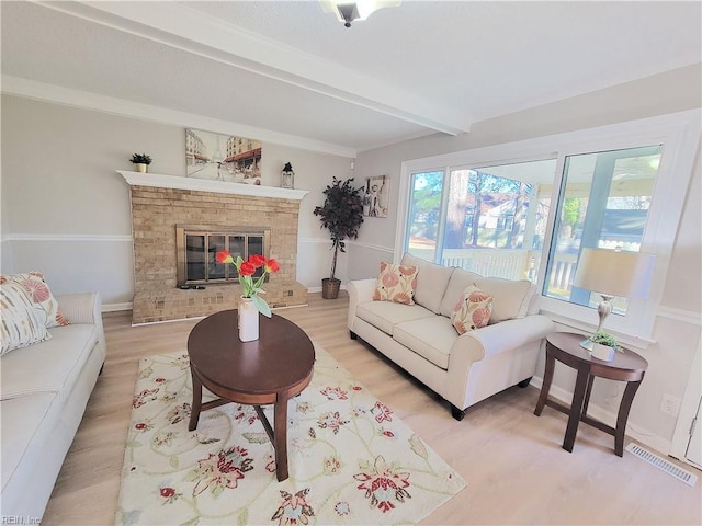 living room with beamed ceiling, light wood-type flooring, and a brick fireplace