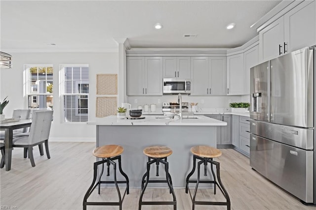 kitchen with stainless steel appliances, a kitchen breakfast bar, gray cabinets, a kitchen island with sink, and ornamental molding