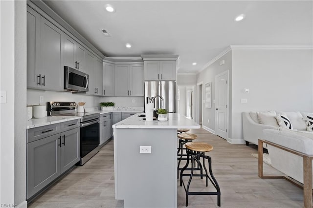 kitchen with a kitchen bar, appliances with stainless steel finishes, a kitchen island with sink, light hardwood / wood-style flooring, and gray cabinets