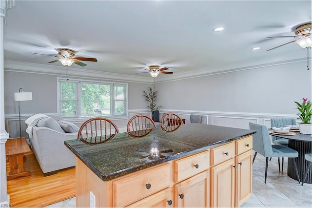 kitchen with light brown cabinets, a kitchen island, crown molding, and dark stone countertops